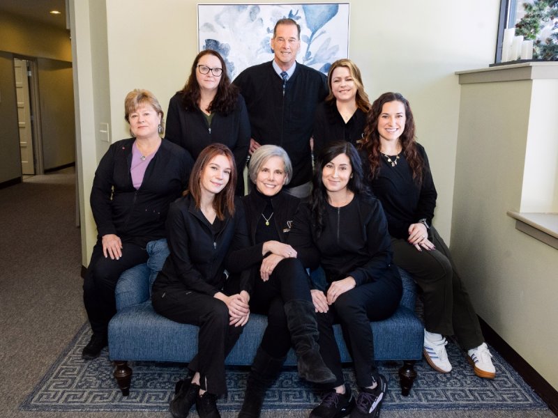 Nine colleagues posing for a group photo on a blue sofa in a bright office lobby.